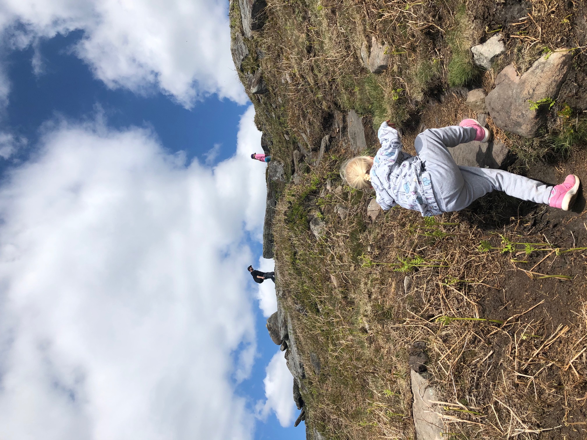 Child climbing a grassy bank on the moors of Stanage Edge, enjoying outdoor play surrounded by rolling Peak District hills